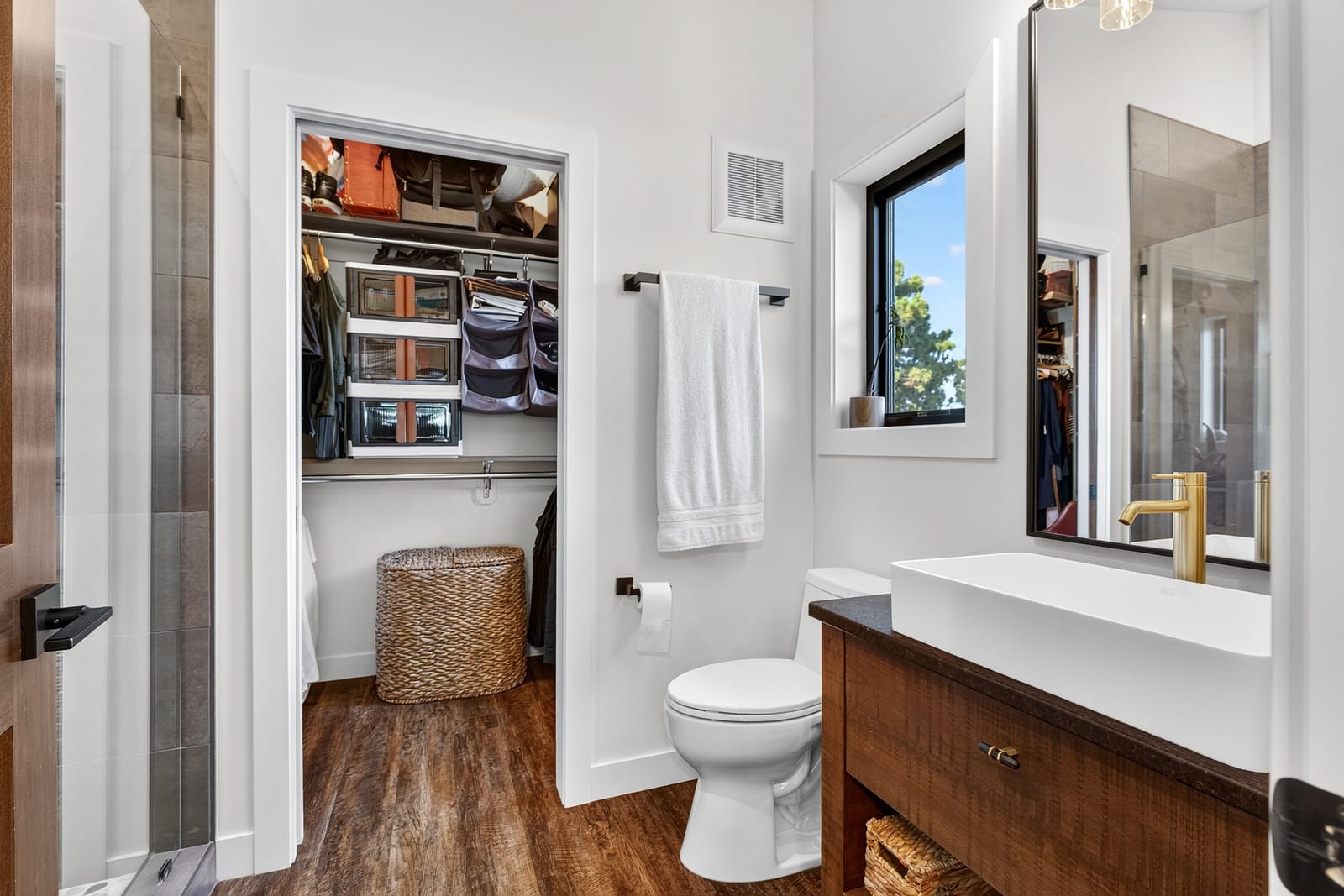 A bathroom with a timber vanity and the walk-in closet beyond.